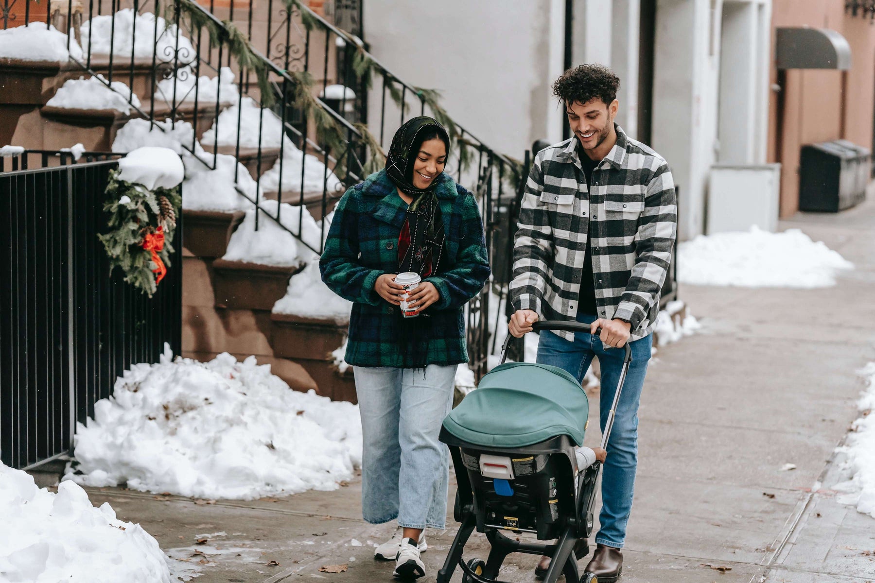 a couple walking their baby in a stroller in the snow 