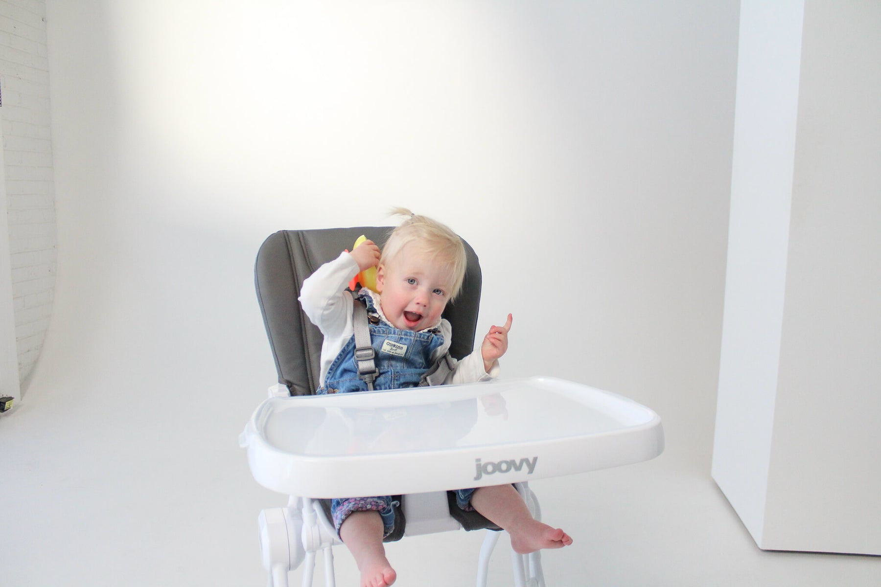 blonde haired little girl sitting in the Joovy high chair smiling