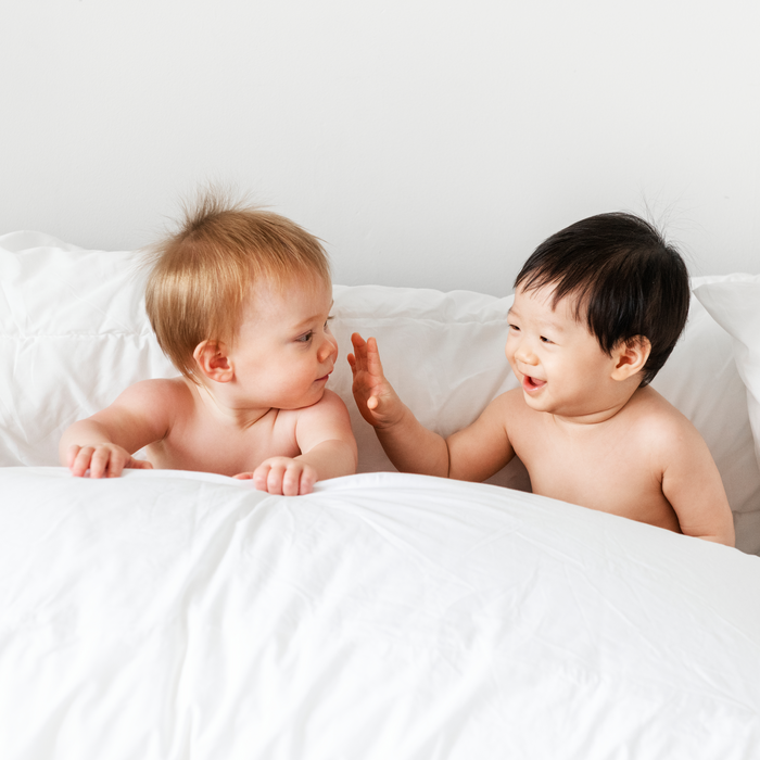 two babies laughing in a bed with white sheets